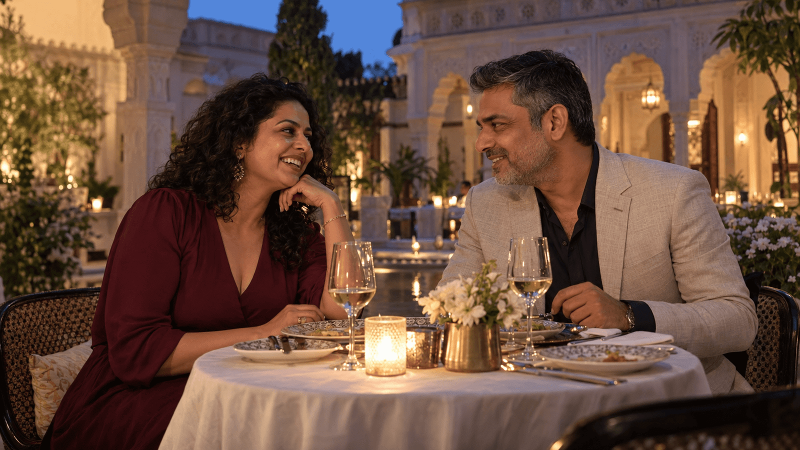 A couple smiling at each other over dinner in a courtyard.